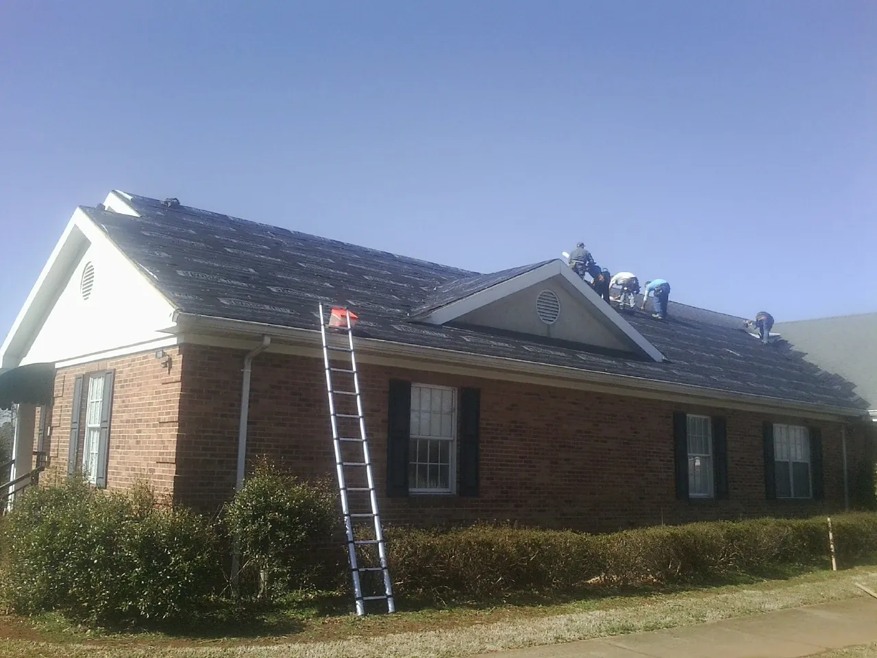 Crew tearing shingles off a brick ranch roof with a ladder set — Metal Roof Repair work by our crew in West Union